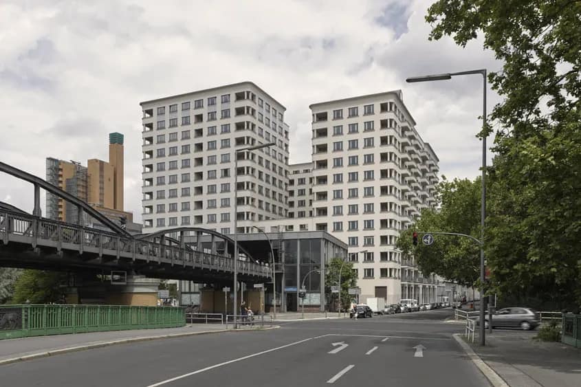 Die beiden hellen Wohntürme von der Straße aus, davor die Stahlbrücke der Hochbahn, links im Hintergrund ein Backsteinhochhaus.