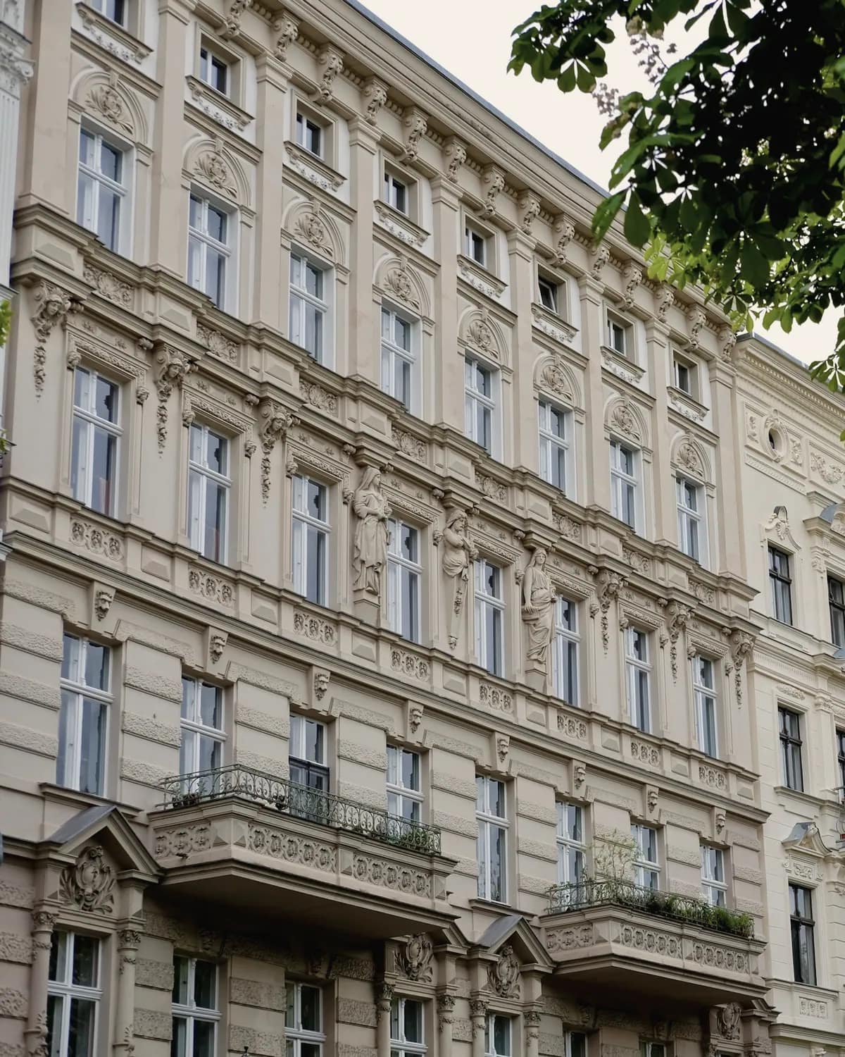 Reich verzierte, helle Gründerzeitfassaden mit Stuck und bepflanzten Balkonen, im Vordergrund Kastanienlaub.